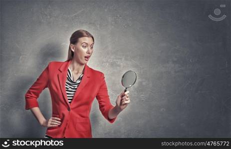 Girl using magnifier for search. Beautiful emotional woman in red jacket looking through magnifying glass