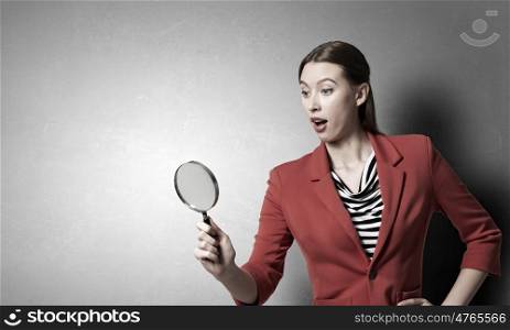 Girl using magnifier for search. Young attractive woman in red jacket looking in magnifying glass