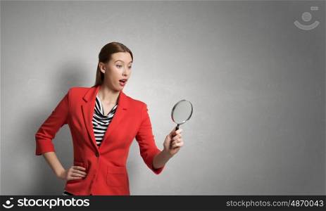 Girl using magnifier for search. Young attractive woman in red jacket looking in magnifying glass