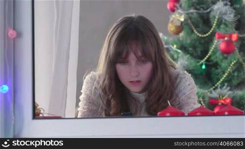 Girl using smart phone near Christmas tree something typing