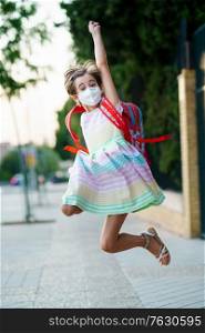 Girl wearing a mask takes a jump for joy at going back to school. Back to school concept.. Girl wearing a mask takes a jump for joy at going back to school.