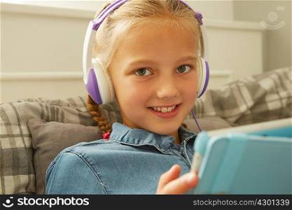 Girl wearing headphones holding digital tablet looking at camera smiling