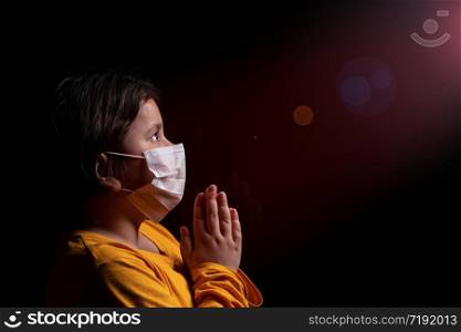 Girl wearing mask for protection against Covid-19 coronavirus pandemic. She is praying God for a cure and help. Copy space.. Girl praying God
