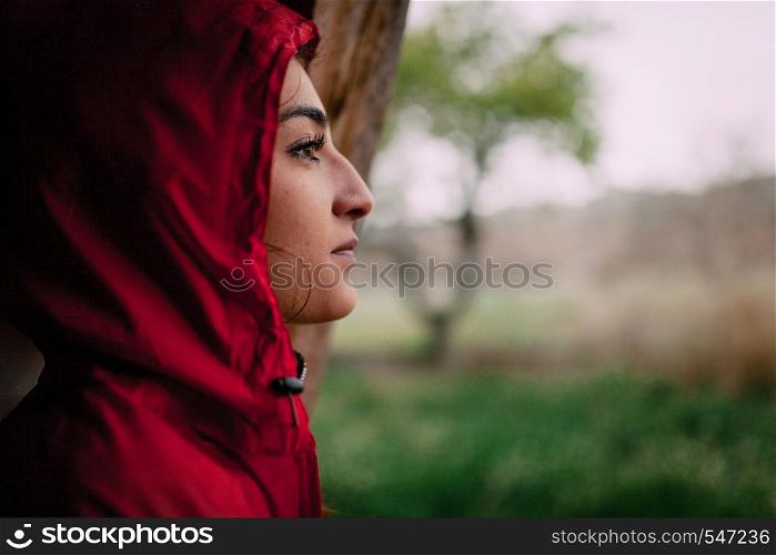 Girl wearing red raincoat observes the rain on the field
