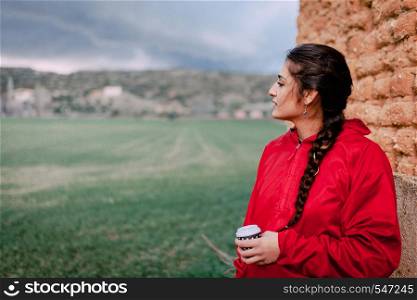 Girl wearing red raincoat observes the rain on the field