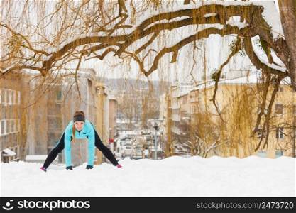 Girl wearing sportswear and doing stretching exercises on snow with urban background. Winter sports, outdoor fitness, fashion, workout, health concept.. Winter workout. Girl wearing sportswear, stretching exercises.