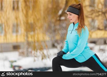 Girl wearing sportswear and doing stretching exercises on snow with urban background. Winter sports, outdoor fitness, fashion, workout, health concept.. Winter workout. Girl wearing sportswear, stretching exercises.
