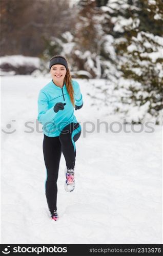 Girl wearing sportswear and running on snow with trees in background, front view. Winter sports, outdoor fitness, workout, health concept.. Running girl wearing sportswear, winter fitness