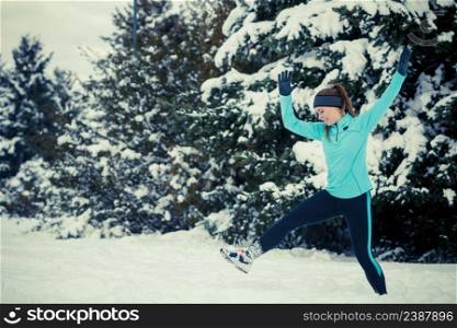 Girl wearing sportswear, trying to do star jump, trees in background. Winter sports, outdoor fitness, workout, health concept.. Girl wearing winter sportswear, trees background