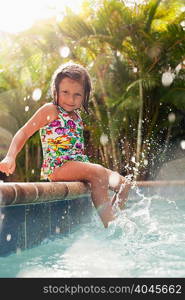 Girl wearing swimming costume sitting on sunlit poolside splashing