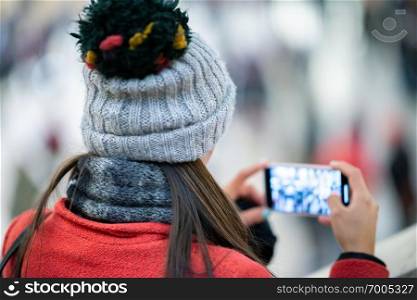 Girl wearing winter hat making pictures with mobile phone inside station.