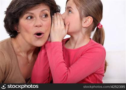 Girl whispering a secret to her grandmother