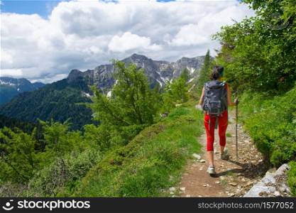 Girl with a backpack and poles during an alpine trekking alone.