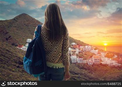 girl with a backpack looking at the city on the coast at sunset. Mountain landscape on tropical island Tenerife