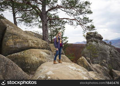 girl with a backpack stands on Dovbush rocks at the Carpathians, Ukraine