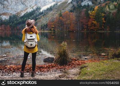girl with a backpack stands on the shore of a mountain lake