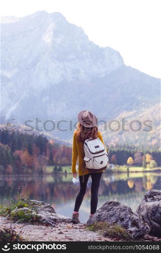 girl with a backpack stands on the shore of a mountain lake