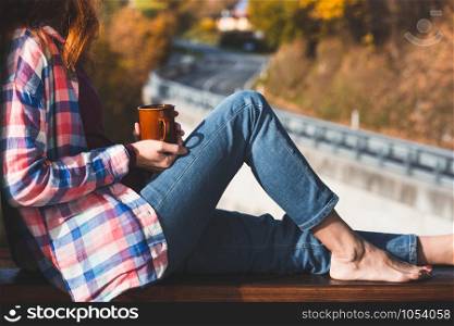Girl with a cup of coffee sitting on the railing on the balcony. morning in a mountain hut
