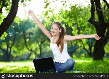 Girl with a laptop in the park with outstretched arms