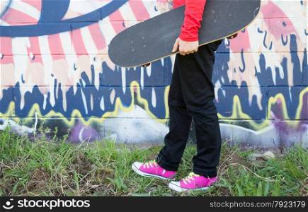 Girl with a skateboard next to a graffiti wall