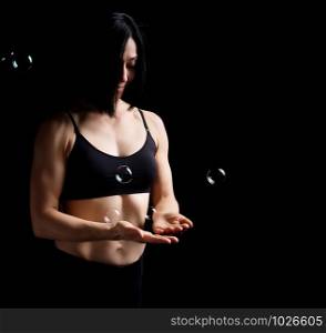 girl with a sports figure and muscles holds a soap bubble in her palm, low key