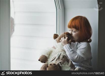 Girl with a toy sitting on the windowsill.. A little girl with red hair plays with toy 4387.