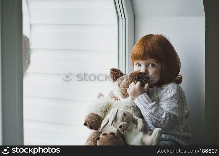 Girl with a toy sitting on the windowsill.. A little girl with red hair plays with toy 4388.