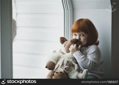 Girl with a toy sitting on the windowsill.. A little girl with red hair plays with toy 4388.
