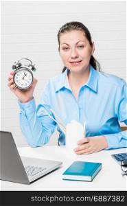 Girl with an alarm clock in a blue shirt in the office at the table