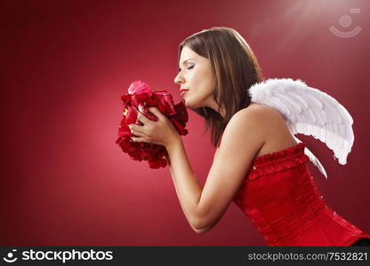 Girl with angelic wings smells petals of the roses, isolated on a red background