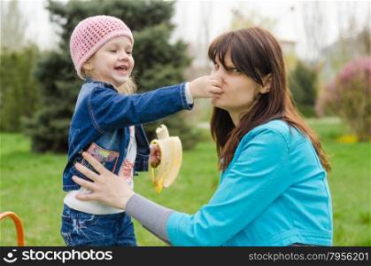 Girl with banana mother pinched nose. Young girl and a three year old at a picnic on a green lawn