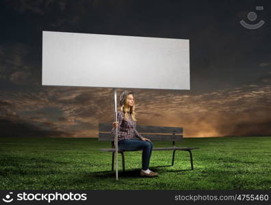 Girl with banner. Young woman in casual sitting on bench and holding white blank banner