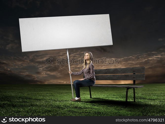 Girl with banner. Young woman in casual sitting on bench and holding white blank banner