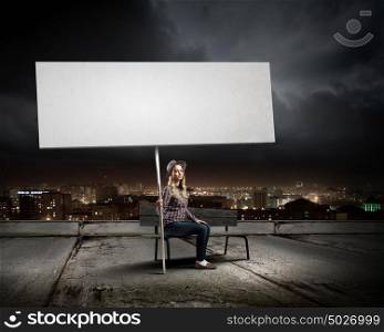 Girl with banner. Young woman in casual sitting on bench and holding white blank banner