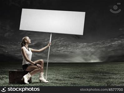 Girl with banner. Young woman with blank banner sitting on suitcase