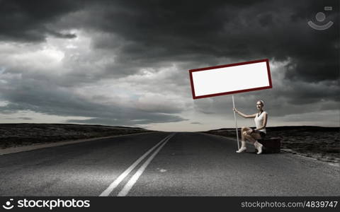 Girl with banner. Young woman with blank banner sitting on suitcase