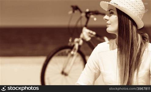 Girl with bike on beach.. Sport and recreation. Young girl in straw hat resting after cycling on beach. Smiling tourist spending time on seaside. Leisure in summer.