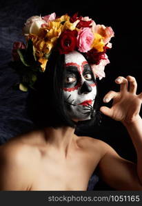 girl with black hair is dressed in a wreath of multi-colored roses and makeup is made on her face Sugar skull to the day of the Dead. Woman looking at the camera, black spider in mouth