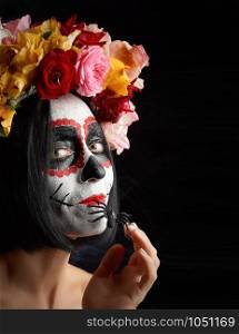 girl with black hair is dressed in a wreath of multi-colored roses and makeup is made on her face Sugar skull to the day of the Dead. Woman looking at the camera