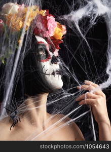 girl with black hair is dressed in a wreath of multi-colored roses and makeup is made on her face Sugar skull to the day of the Dead