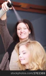 Girl with blond wavy hair by hairdresser. Hairstylist with hairspray and female client. Young woman in hairdressing beauty salon. Hairstyle.