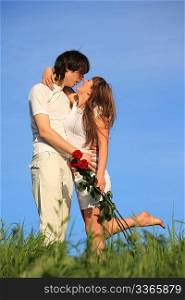 girl with bouquet of roses kisses guy on grass against sky