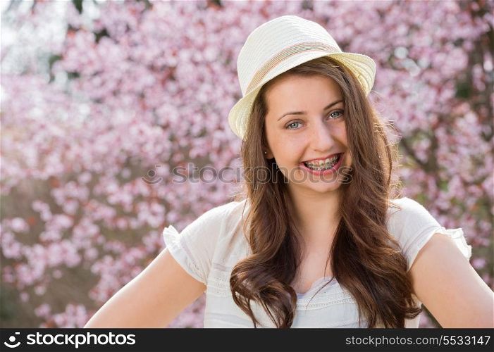 Girl with braces wearing hat in front of blossom tree