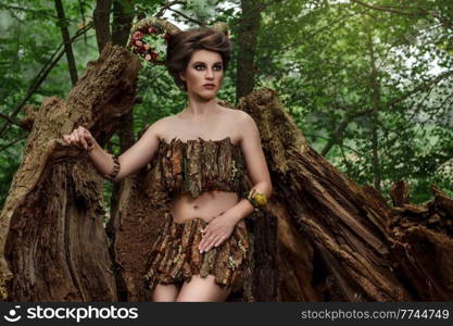 girl with braided horns in a dress made of bark on a forest path near the fallen trees