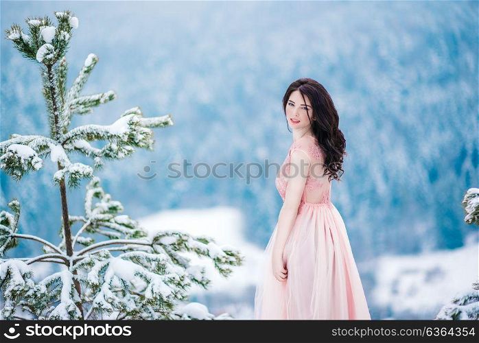girl with brown hair, blue eyes and a pink dress on the background of the winter mountains