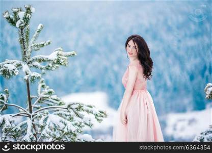 girl with brown hair, blue eyes and a pink dress on the background of the winter mountains