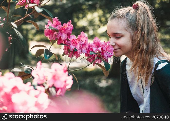 Girl with closed eyes standing in garden among the flowers, smelling beautiful pink flower