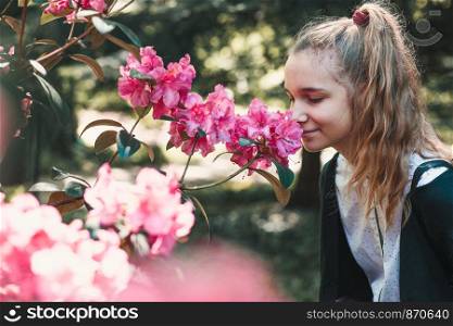 Girl with closed eyes standing in garden among the flowers, smelling beautiful pink flower
