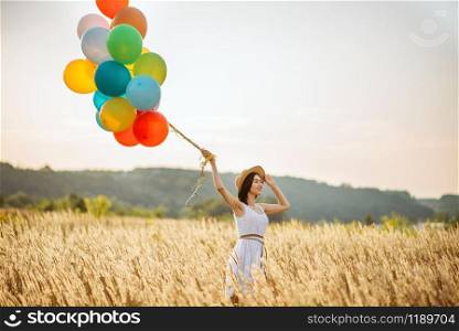 Girl with colorful air balloons in a rye field. Pretty woman on summer meadow