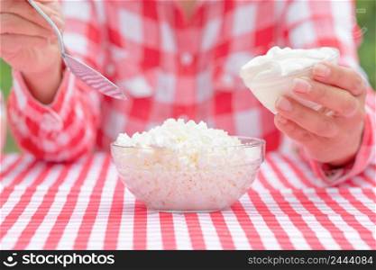 Girl with cottage cheese and sour cream. The girl&rsquo;s hands in a checkered shirt are holding a loka and a saucer of sour cream. There is a bowl of cottage cheese on the table. Girl with cottage cheese and sour cream